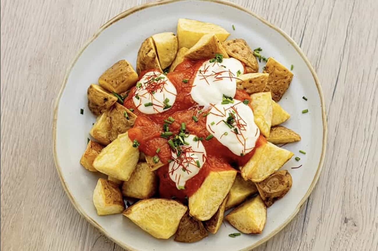 Le meilleur restaurant du monde est en Espagne (selon TripAdvisor) 2 Frites croustillantes avec sauce tomate, œufs pochés et herbes fraîches, servies sur une assiette blanche. Parfait pour une expérience culinaire en Espagne.