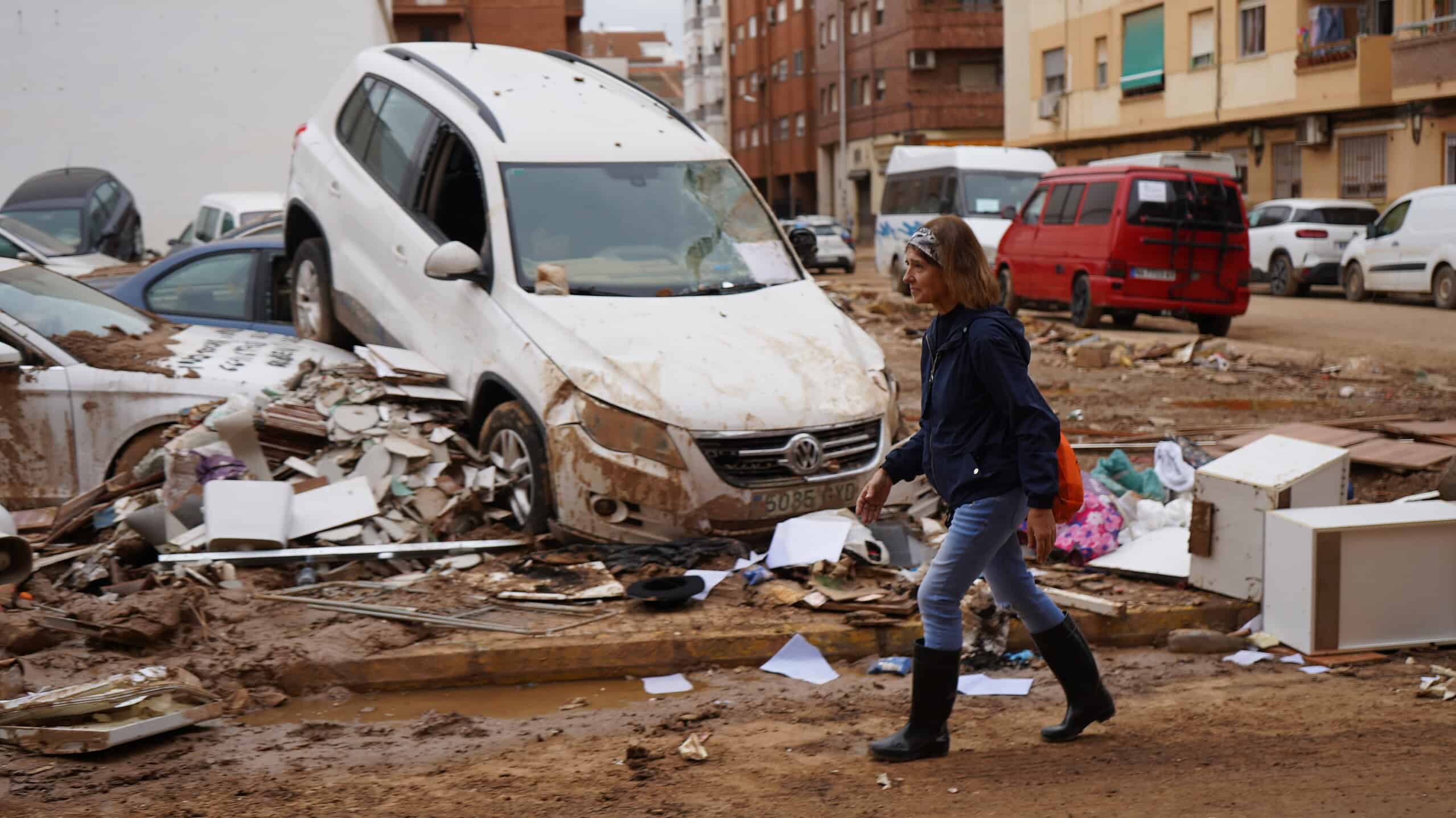 Femme marchant à travers un paysage de débris et de véhicules endommagés suite aux inondations à Valence, illustrant la destruction causée par la catastrophe naturelle.