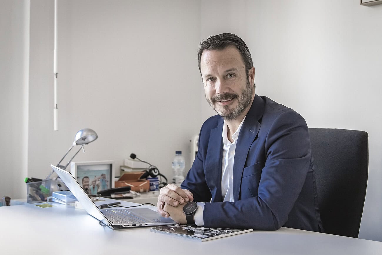 Homme avocat en réunion de travail dans un bureau moderne, portant un costume bleu, avec un ordinateur portable et des documents, illustrant la profession juridique en contexte professionnel.