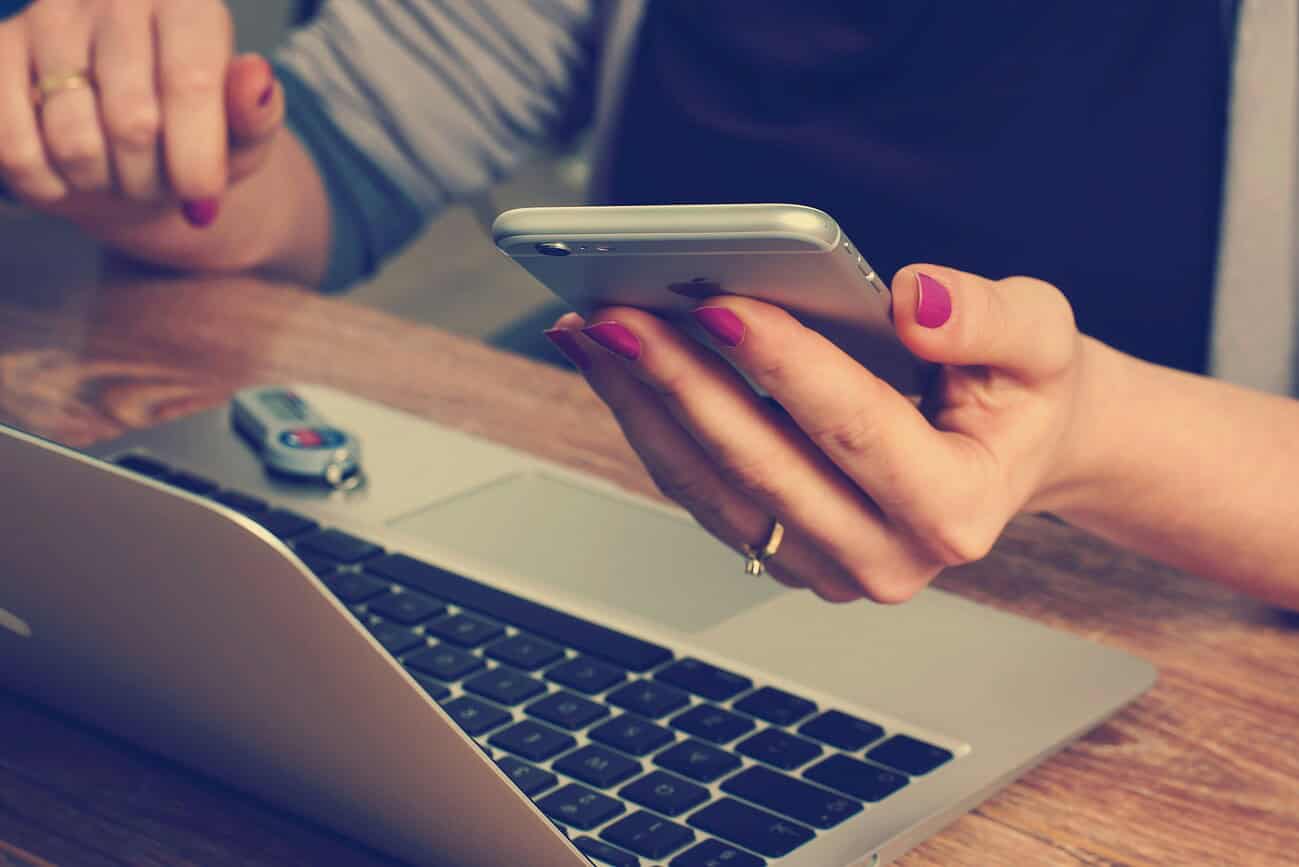 Personne utilisant un smartphone avec un ordinateur portable et une clé USB sur un bureau, illustrant la transformation des attentes des consommateurs grâce à la décentralisation.