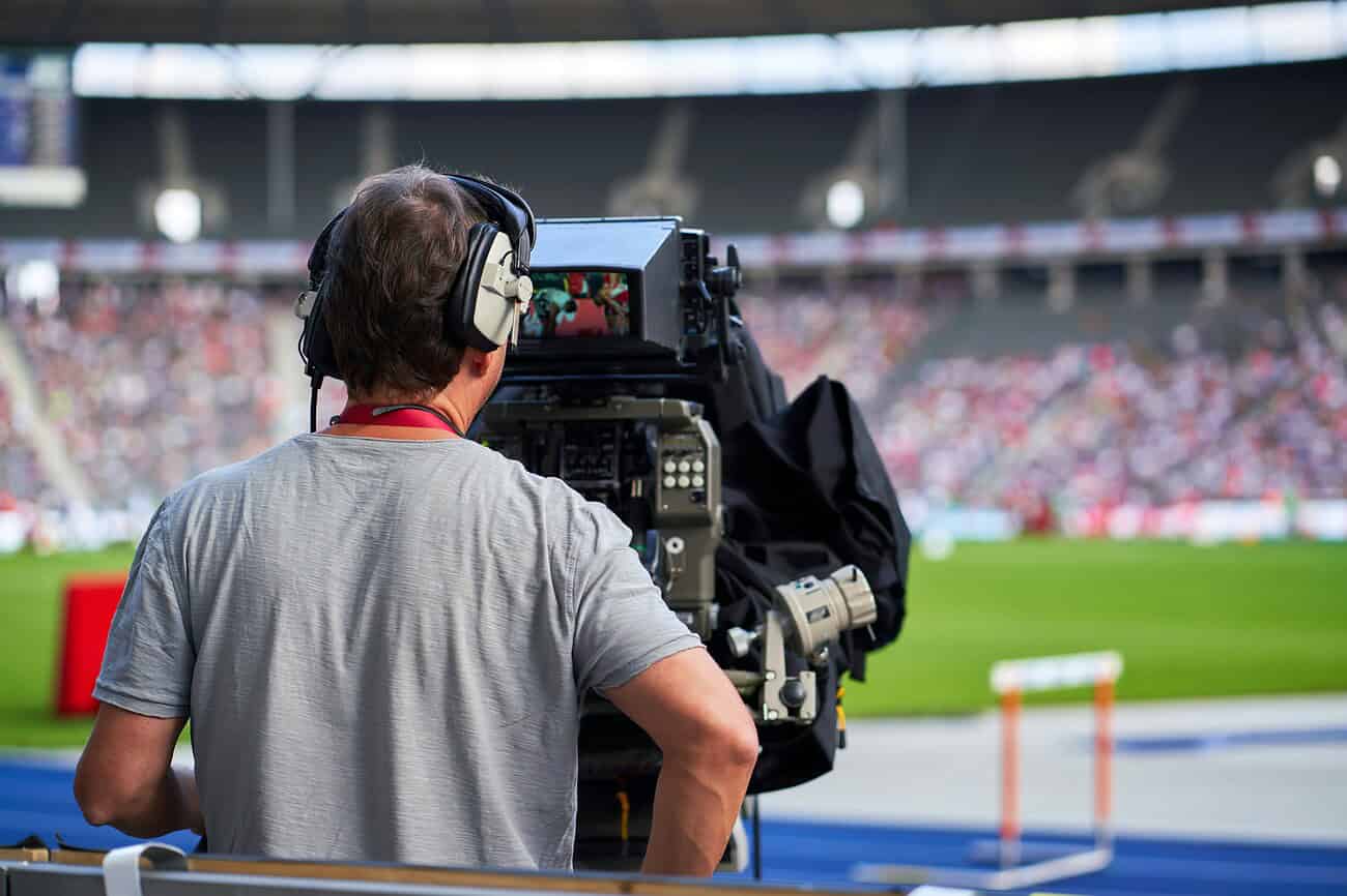 Caméraman professionnel enregistrant un événement sportif en direct dans un stade rempli de spectateurs.