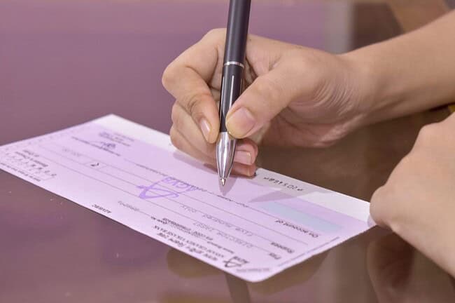 Personne en train de signer un chèque bancaire, illustrant l'absence de chèques en Espagne.