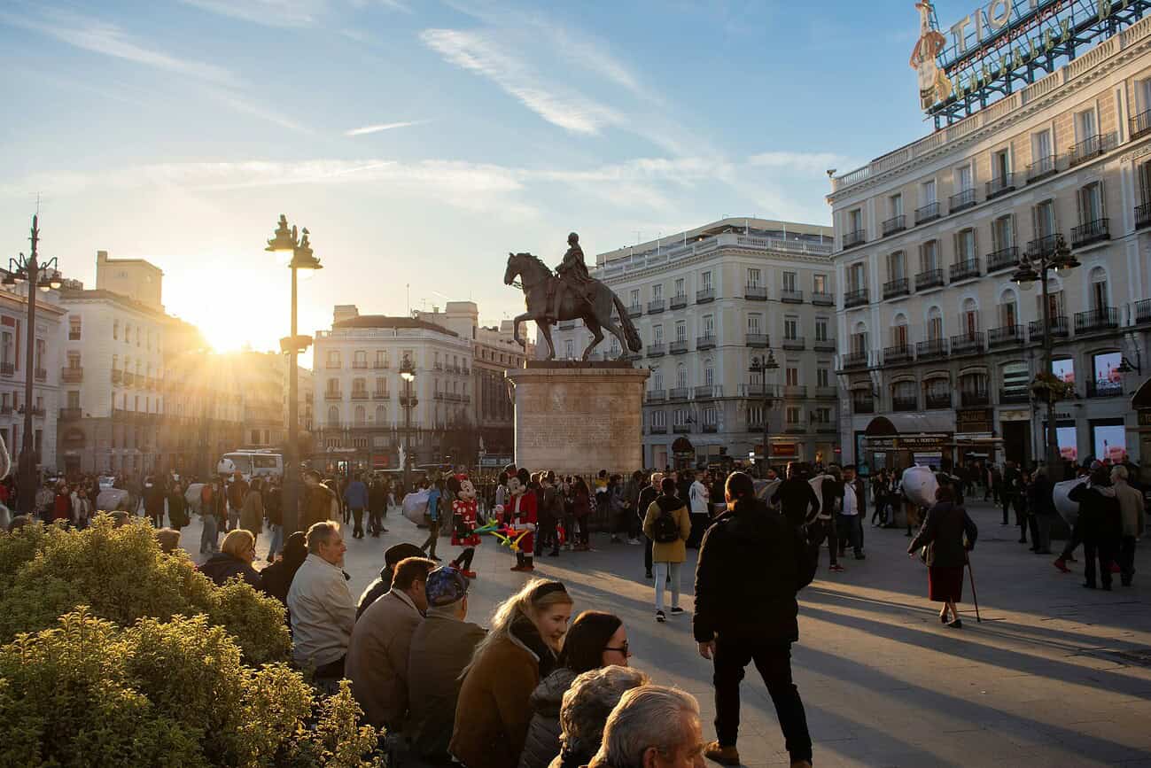 Étalage de la vie urbaine à Madrid avec une foule de passants et une statue emblématique au coucher du soleil.
