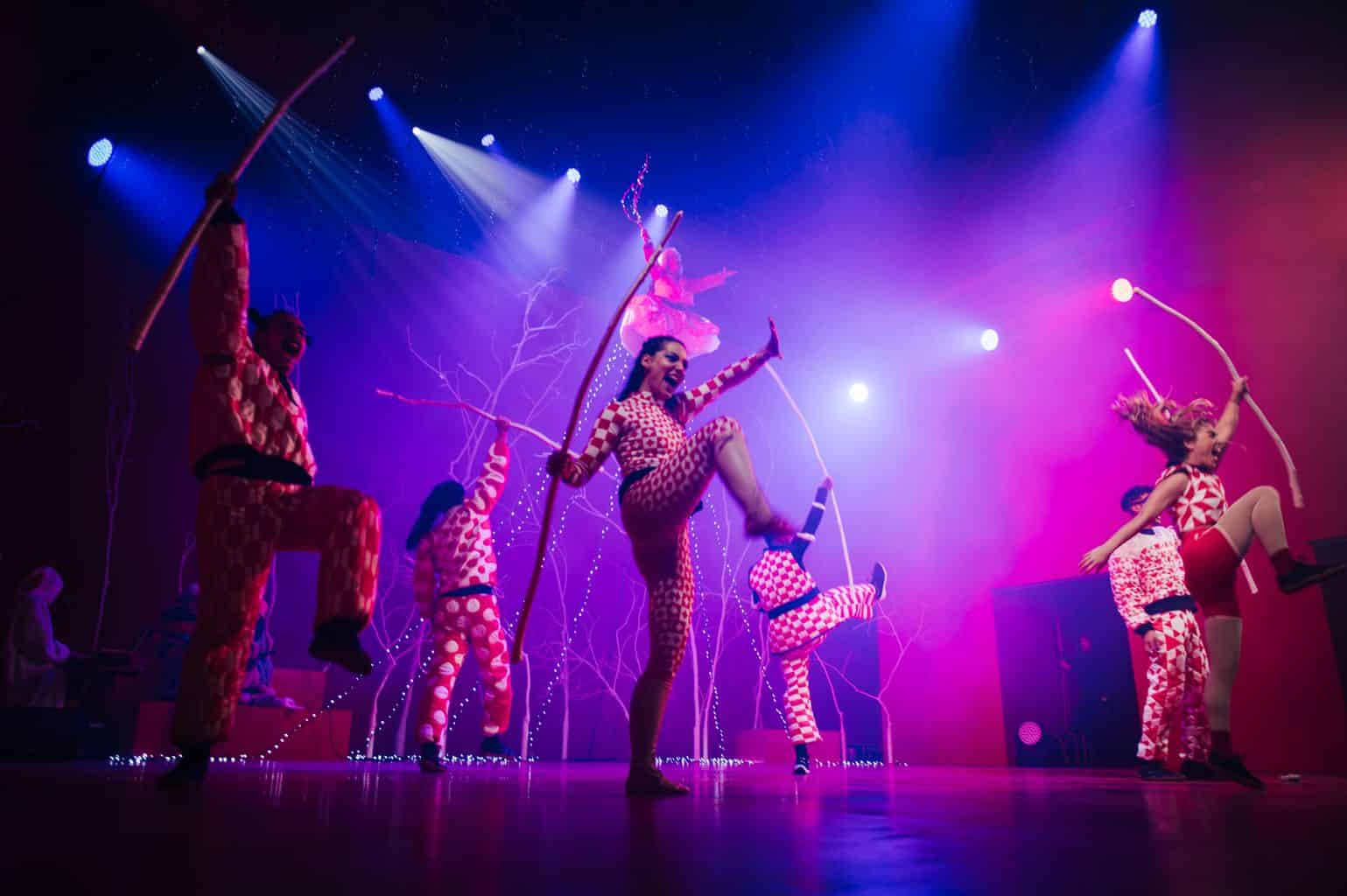 Équinox, spectacle de cirque avec artistes en costumes colorés et acrobates utilisant des bâtons lumineux, dans une ambiance lumineuse vibrante.