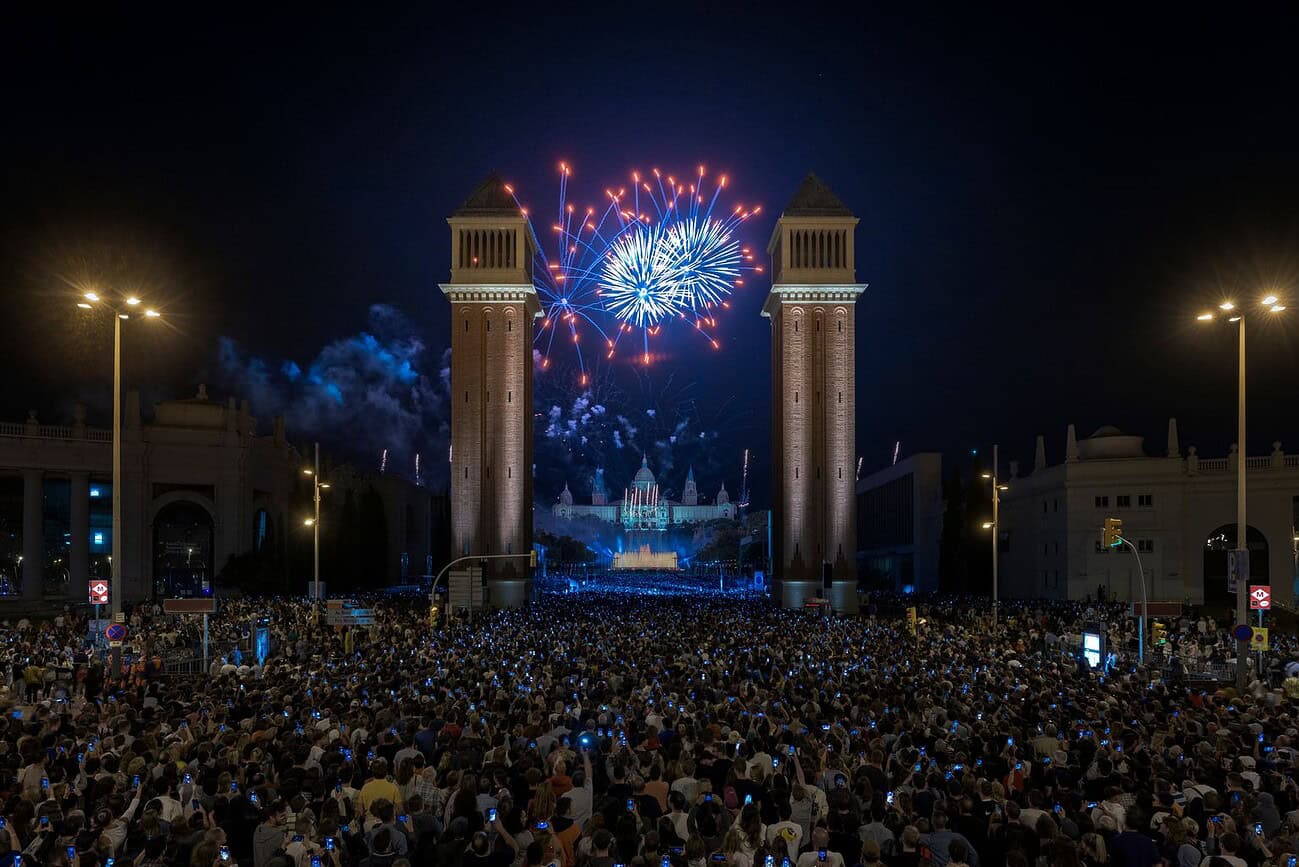 Nouvel An à Barcelone : feu d’artifice, drones et infos pratiques 3 Spectacle de feux d'artifice et drones illuminant le ciel lors du Nouvel An à Barcelone, avec une foule nombreuse réunie devant les célèbres portes de la ville.