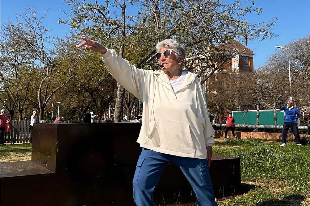 Femme âgée pratiquant le tai-chi dans un parc ensoleillé, illustrant un mode de vie sain et actif pour favoriser la longévité.