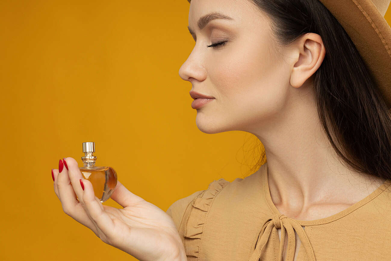 Ces odeurs qui nous suivent partout 1 Femme parfumant son cou avec un flacon de parfum, mettant en valeur la sensuelle odeur qui la suit partout, évoquant la mémoire olfactive et l'importance des fragrances dans notre quotidien.