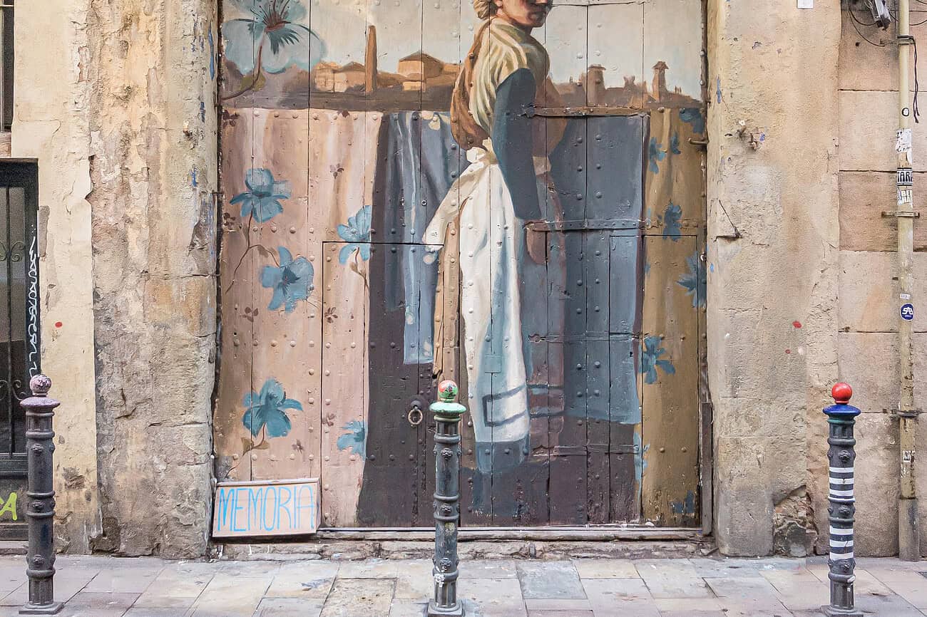 Barcelone : la plus ancienne des rues commerçantes graffée pour ses 1000 ans 3 Sculpture murale représentant une femme en robe, peinte sur une porte en bois dans une rue historique de Barcelone, illustrant l'art urbain et la richesse culturelle de la ville.