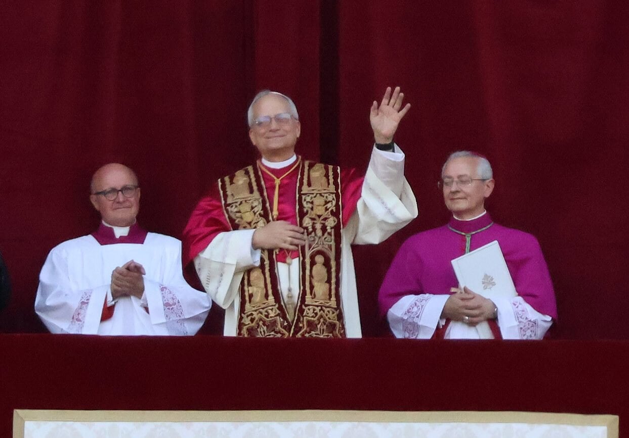 Le pape lors d'une bénédiction à Barcelone, entouré de deux prêtres, devant un fond rouge, célébrant une cérémonie religieuse importante.