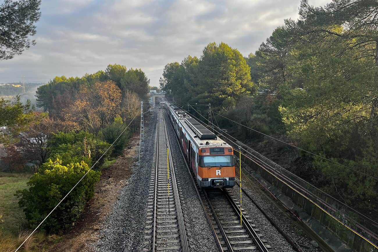 La Catalogne relance son train circulaire autour de Barcelone 2 Train de banlieue en mouvement sur une voie ferrée entourée de végétation, illustrant la paralysie des transports en Catalogne due à la grève.