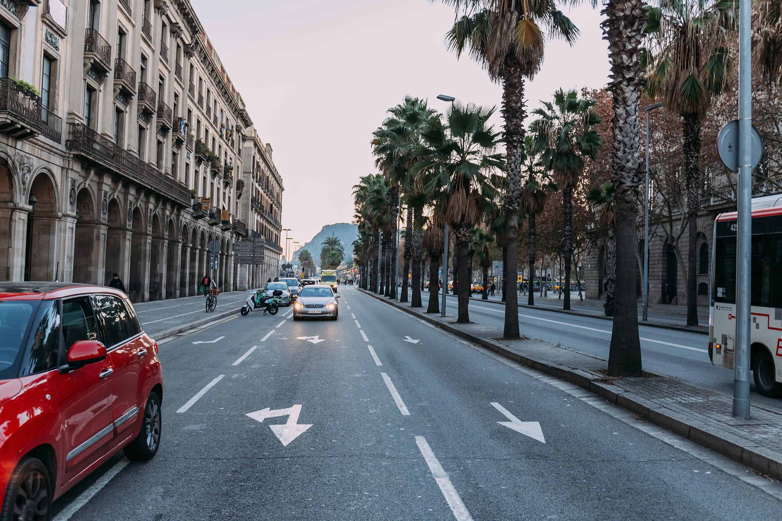 Voiture à Barcelone sur une avenue bordée de palmiers, avec plusieurs véhicules en circulation et un environnement urbain typique de la ville catalane.