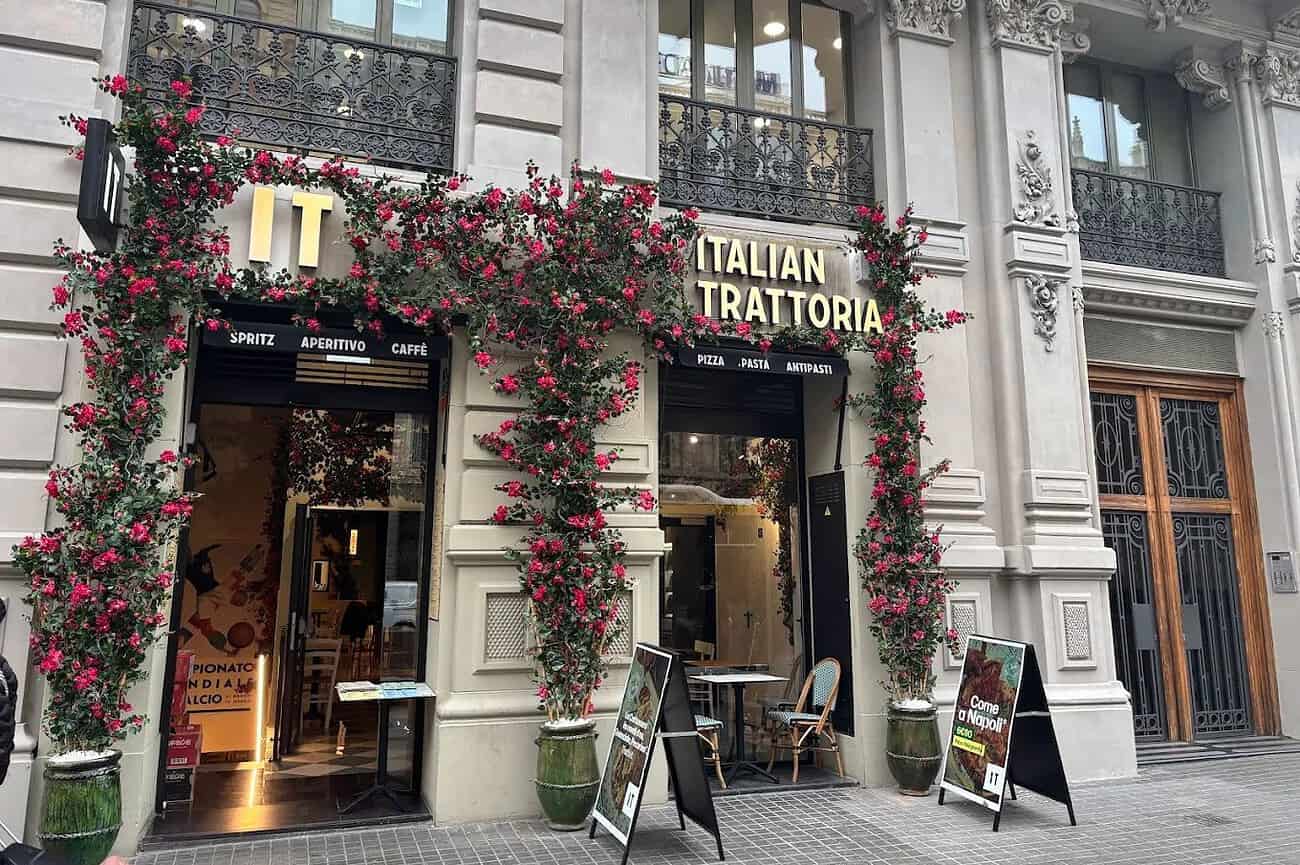 Trattoria Italienne authentique avec façade florale colorée, située dans un bâtiment historique à Barcelone, proposant une cuisine italienne festive et conviviale.