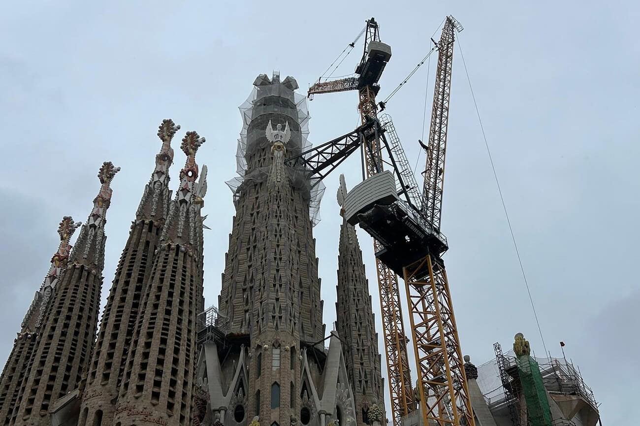 Sagrada Familia en construction avec un ciel orageux et un grue en premier plan, illustrant les défis climatiques et architecturaux liés à la célèbre basilique de Barcelone.