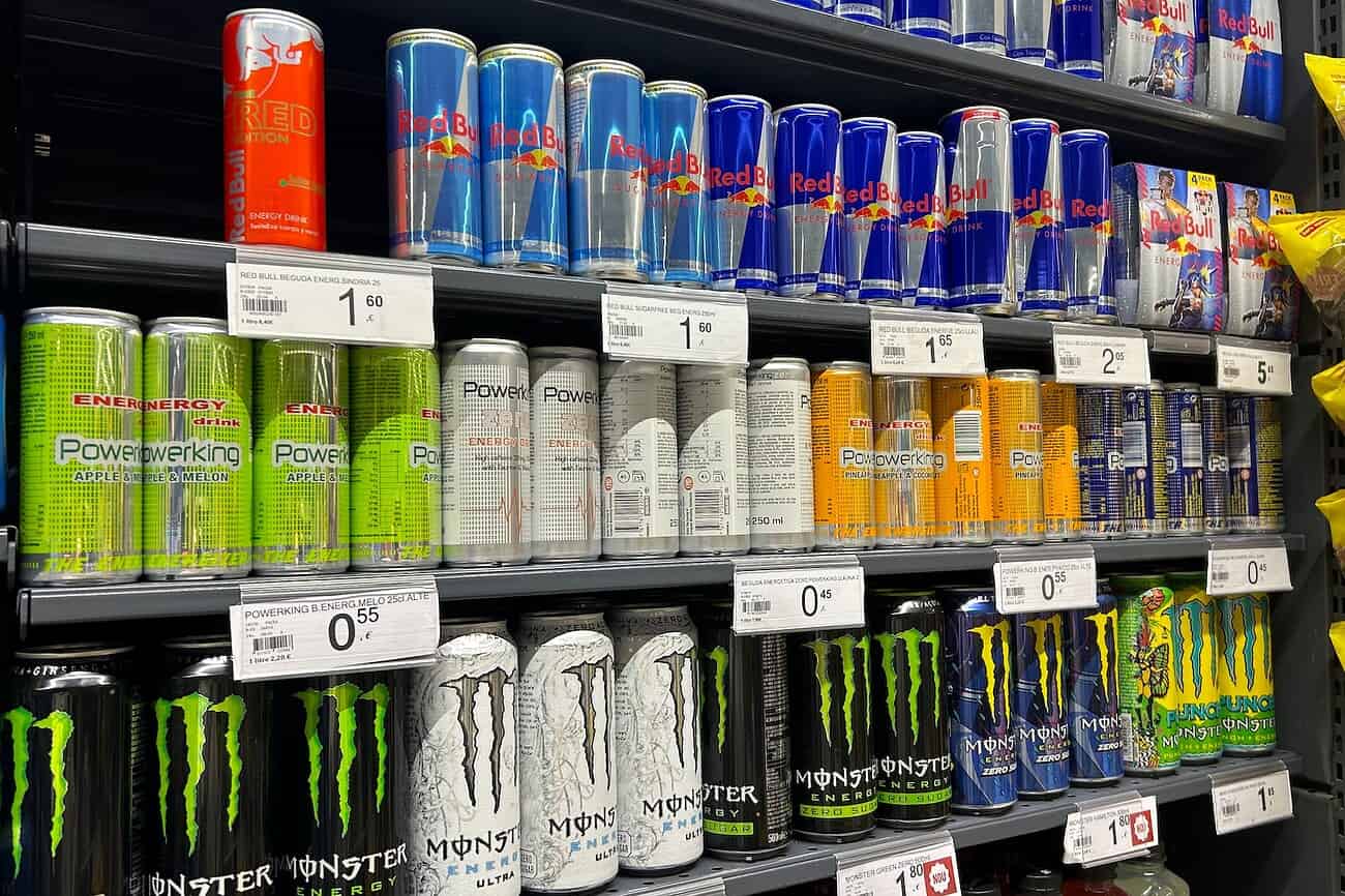 Rayonnage de canettes de boissons énergisantes, notamment Red Bull, Monster et Powerade, dans un supermarché, avec étiquettes de prix visibles.