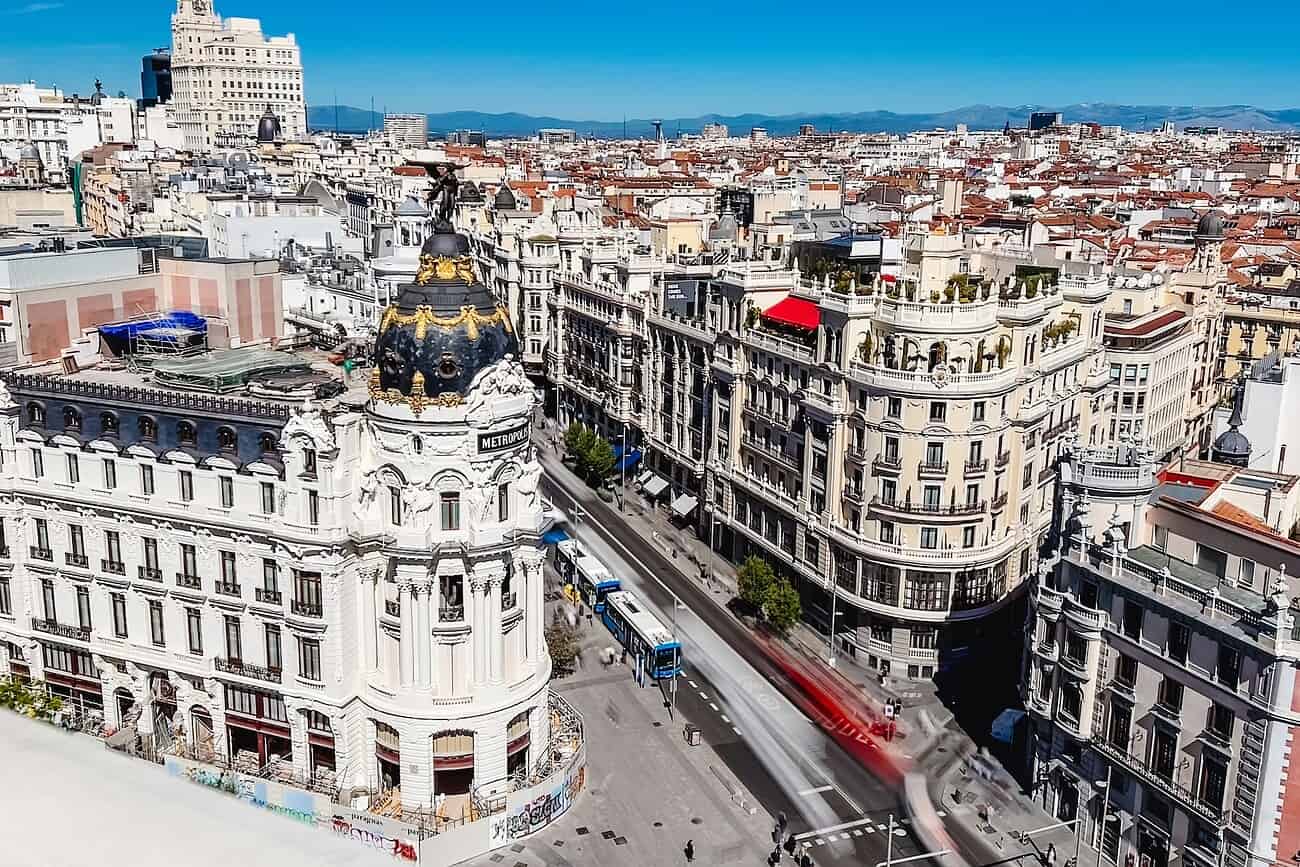 Vue aérienne de Madrid, mettant en valeur l'architecture classique et moderne, avec un tramway rouge traversant la rue principale sous un ciel clair.