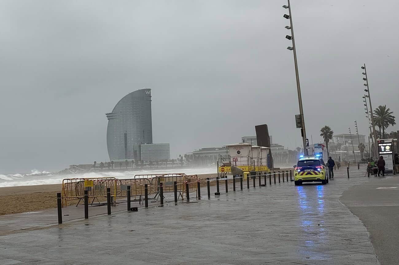 Plage de Barcelone par temps pluvieux avec des vagues, un ciel nuageux et une promenade vide, mettant en valeur l'atmosphère humide et venteuse de la côte méditerranéenne.