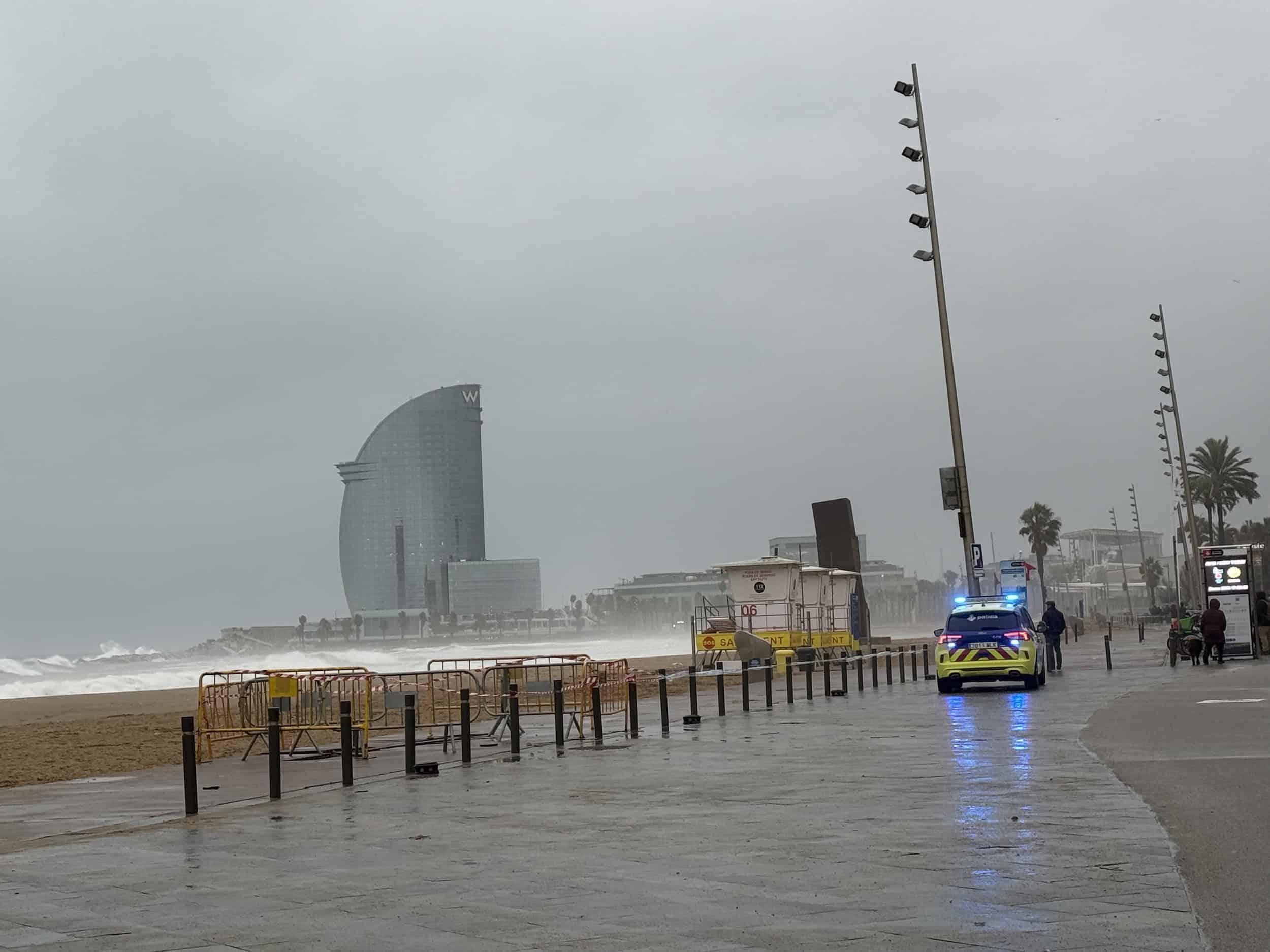 Plage de Barcelone par temps pluvieux avec des vagues, un ciel nuageux et une promenade vide, mettant en valeur l'atmosphère humide et venteuse de la côte méditerranéenne.