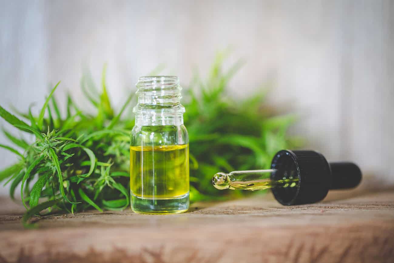 Huile de CBD en bouteille avec plante de cannabis en arrière-plan.
