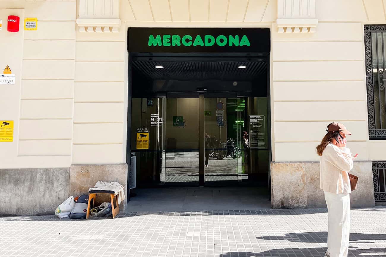 Pourquoi Mercadona est le supermarché préféré des Espagnols (et des Français d'Espagne) 1 Balayage de l'entrée du supermarché Mercadona à Madrid, avec une femme portant un masque et un sac à la main, sous un bâtiment historique.