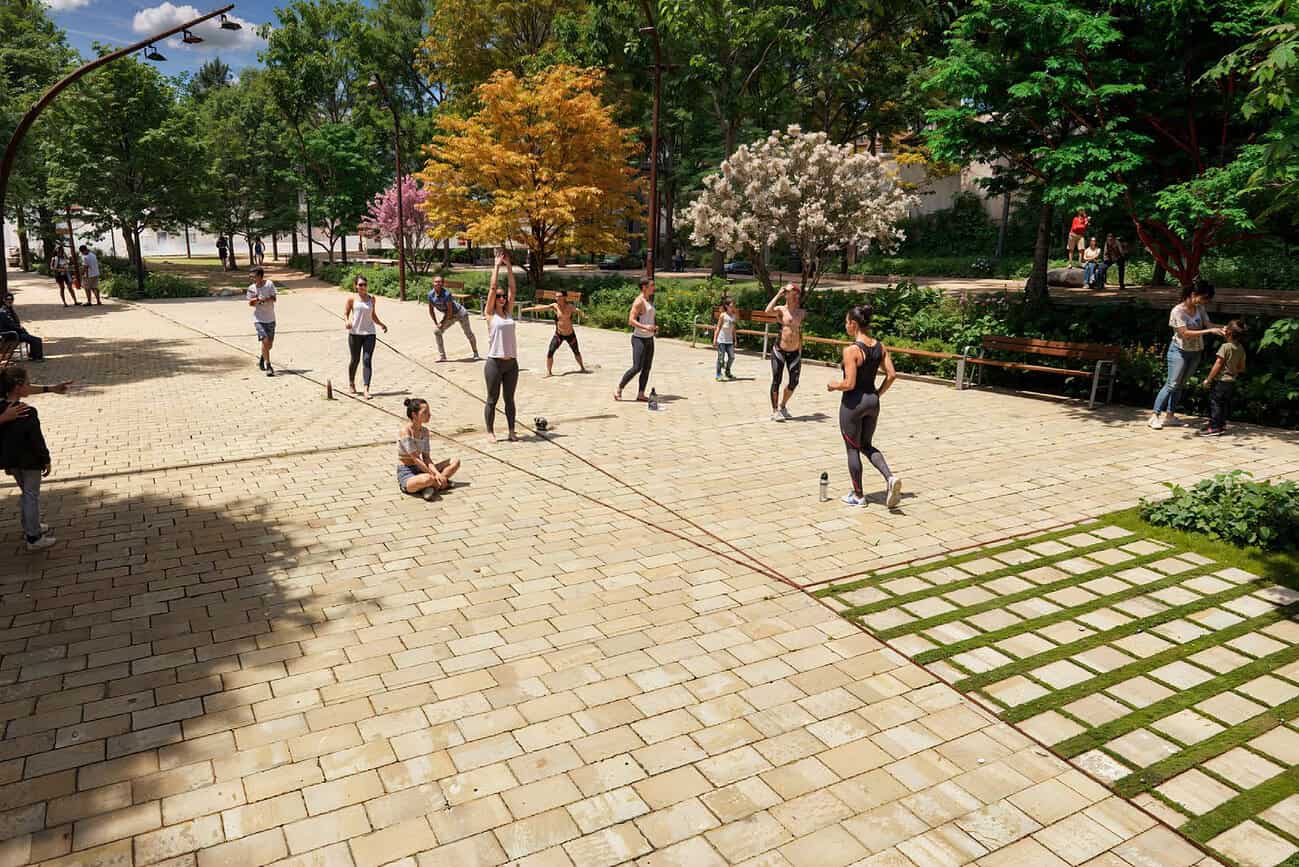 Enfants et adultes jouent à la corde à sauter dans un espace public transformé en jardin à Barcelone, avec arbres et espaces verts, illustrant la reconversion de friches en lieux de convivialité.