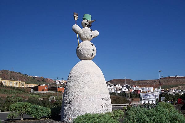 Statue artistique représentant un bonhomme de neige avec un chapeau vert, situé dans un espace urbain en Espagne.