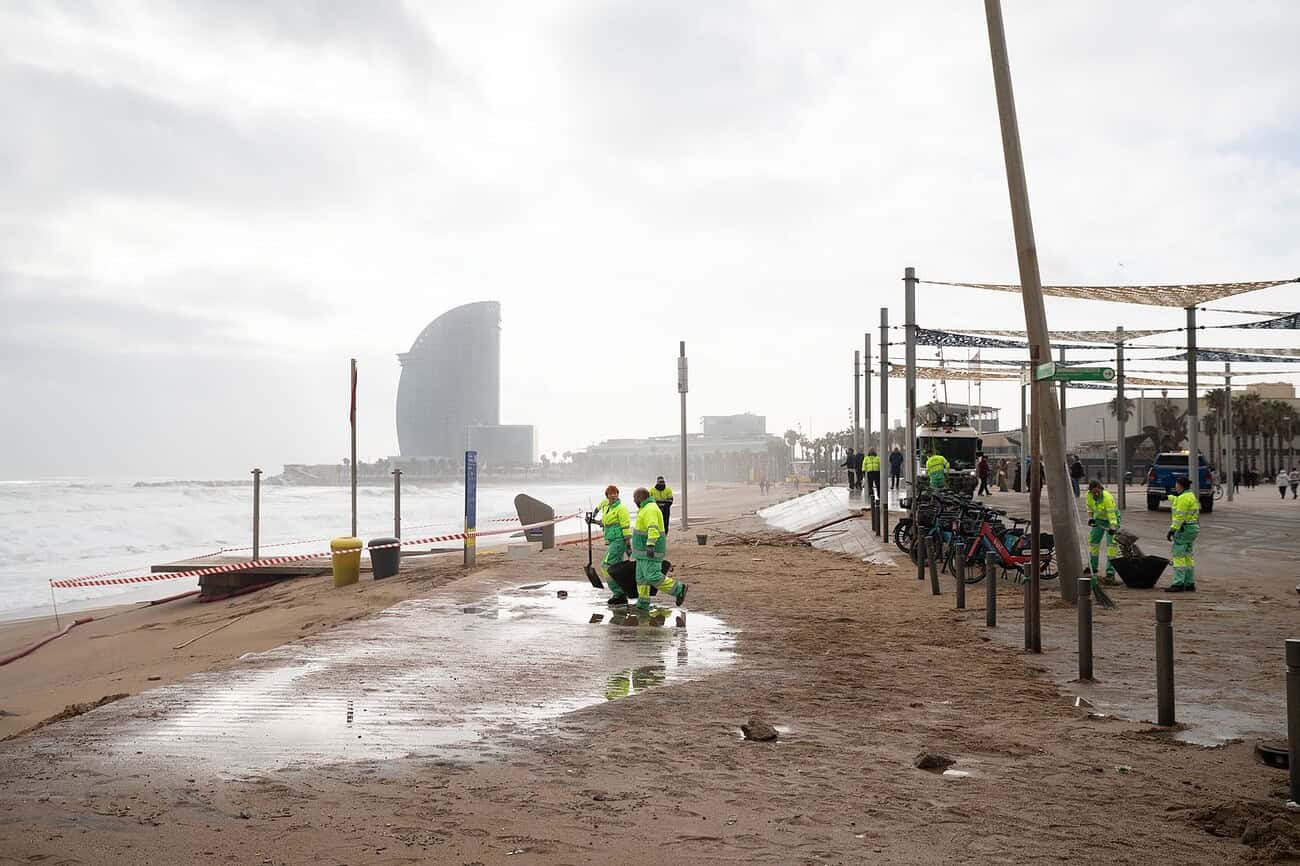 Catalogne : un hiver parmi les moins ensoleillés depuis plus de 15 ans 2 Vue de la plage de Barcelone avec des travailleurs en sécurité, bâtiments modernes et activités urbaines, illustrant le développement technologique et urbain dans la capitale de l'IA.