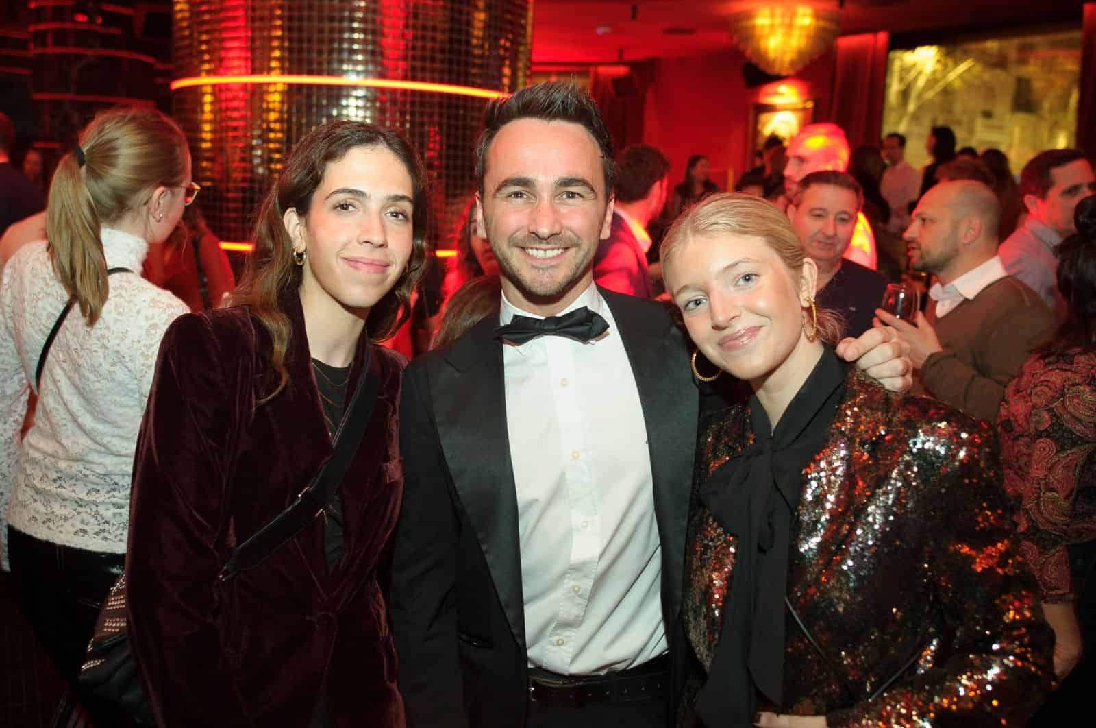 Photo de trois personnes souriantes lors d'une soirée festive à Madrid, avec ambiance chaleureuse et décorations lumineuses.