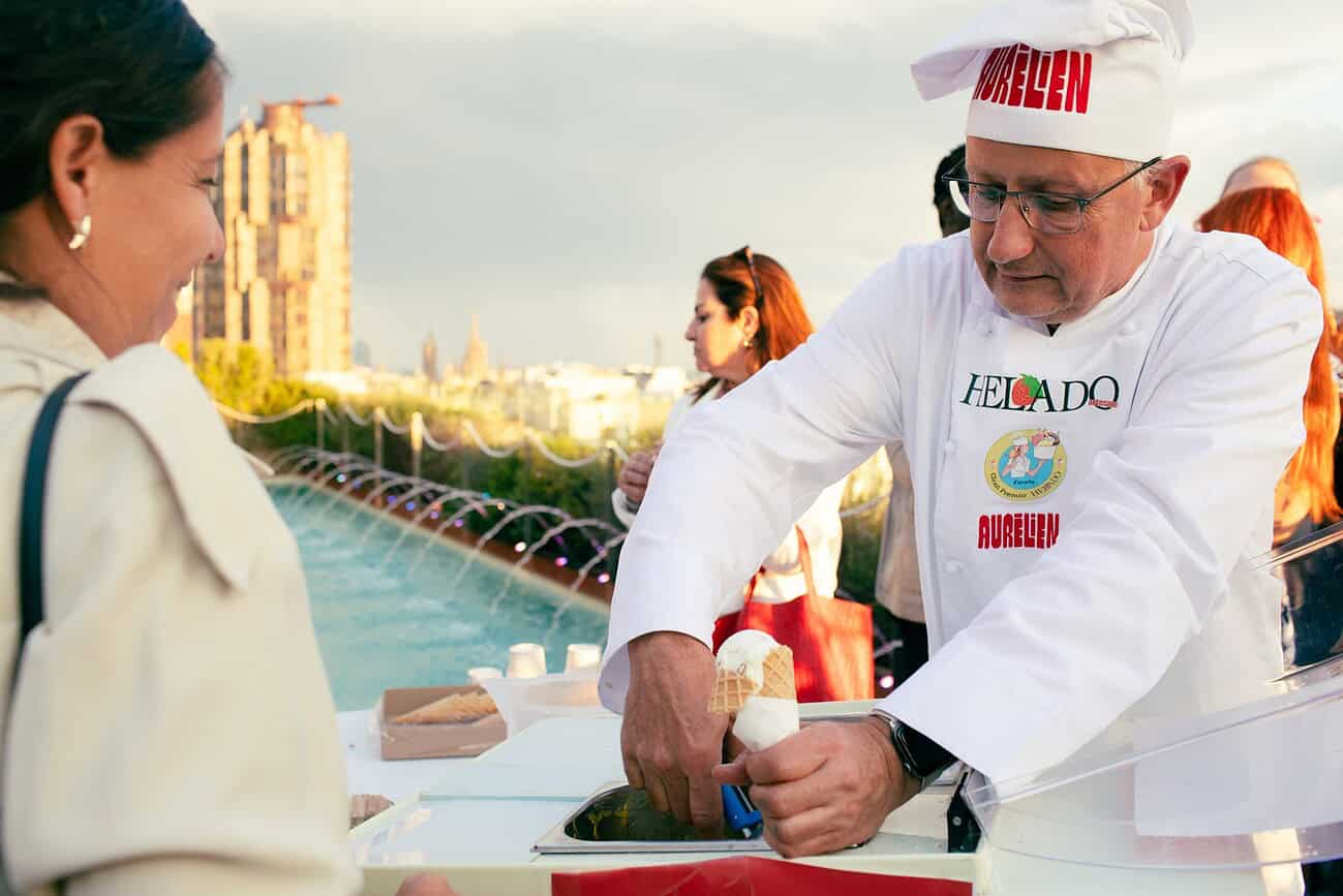 Artisan glacier français préparant une glace artisanale lors d'un événement en plein air à Barcelone, avec la ville en arrière-plan.