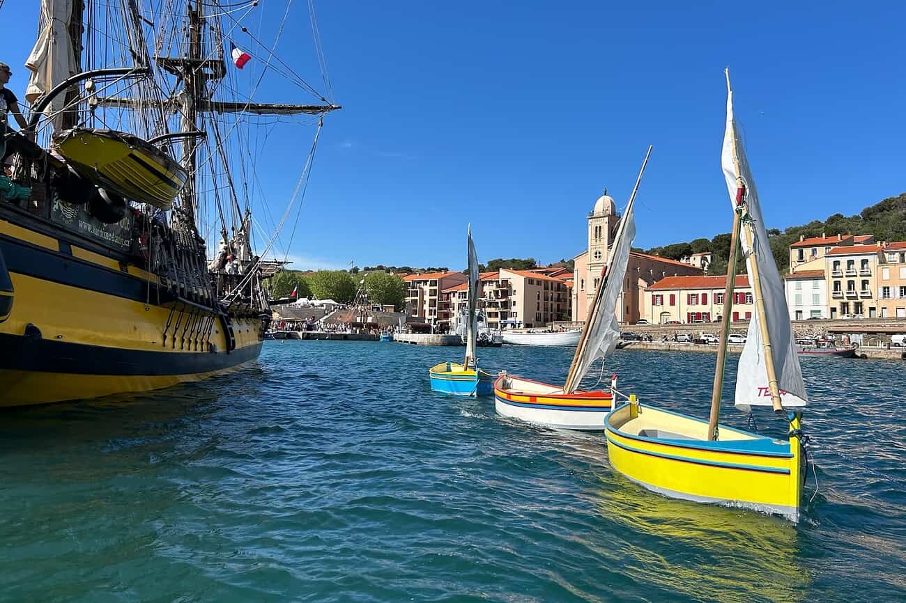 Voiliers colorés dans le port de Port-Vendres, avec un vieux navire en arrière-plan et la ville méditerranéenne ensoleillée.