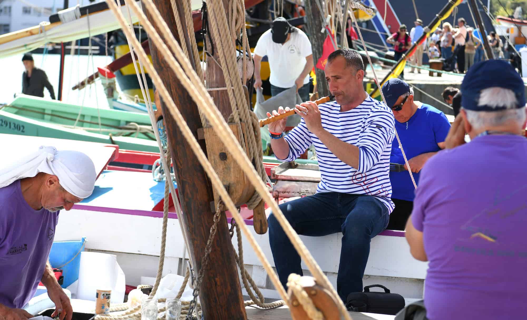 Groupe de marins préparant un voilier lors d'une fête maritime à Port-Vendres, avec plusieurs personnes en activité sur le port.