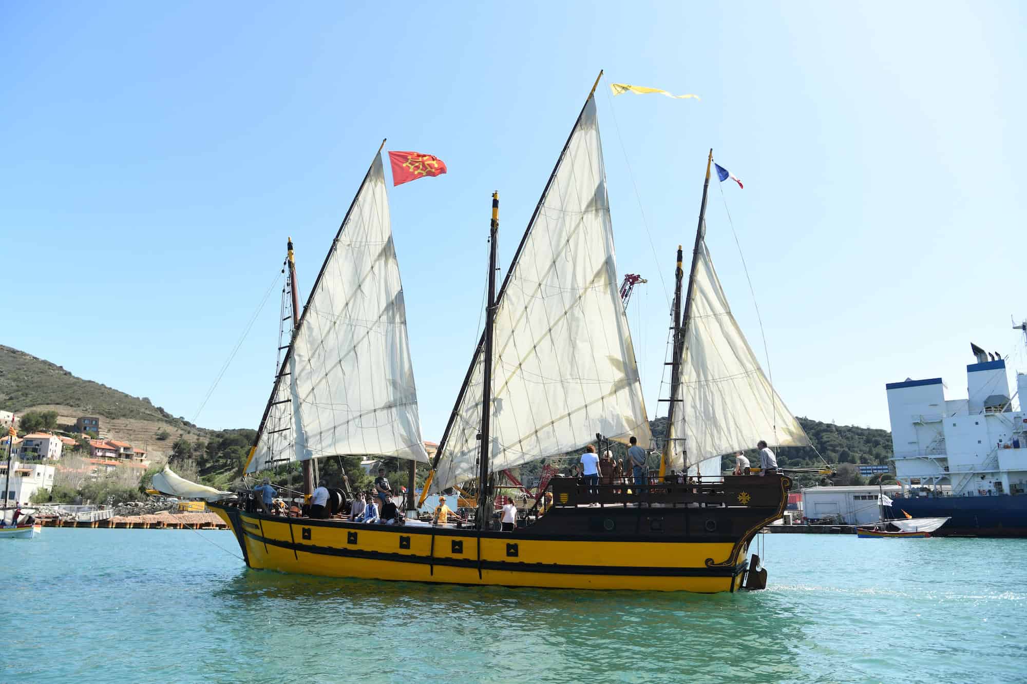 Voilier traditionnel naviguant dans le port de Port-Vendres, avec ses voiles déployées sous un ciel clair.