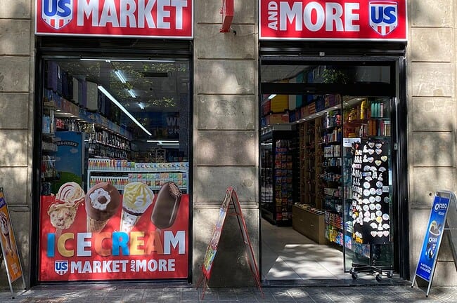Supermarché 24h US et Plus à Barcelone, avec enseignes lumineuses et rayons bien fournis, offrant une large gamme de produits pour les habitants et les visiteurs.